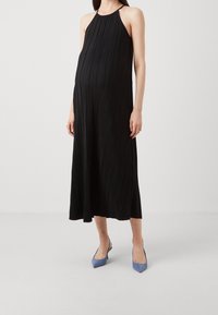 Czarna, plisowana maxi sukienka z dekoltem w kształcie halter, o luźnym kroju. Noszona z niebieskimi czółenkami w szpic.