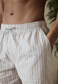 Pantalons de détente rayés en bleu clair et crème, dotés d'une taille élastique avec cordon de serrage et de poches latérales. Texture douce.