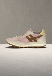 Πλευρική όψη ενός sneaker χαμηλής κοπής με μπεζ, ροζ και καφέ πάνελ, κίτρινη ταμπελίτσα στη φτέρνα, λευκή σόλα και πέλμα από καουτσούκ.