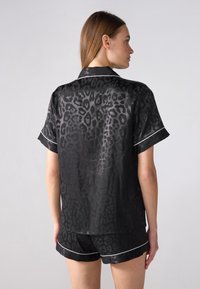 Ensemble de pyjama en satin noir avec un motif léopard, manches courtes et un passepoil blanc. Le haut a une coupe décontractée avec un ourlet arrondi.