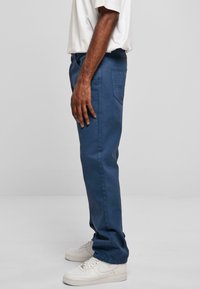 Pantalons en coton bleu à coupe droite avec poches latérales, portés avec des baskets blanches. Texture lisse, présentant un design classique de ceinture.
