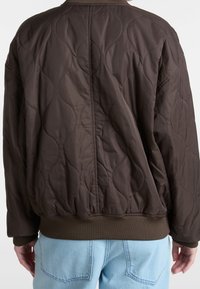 Brązowa pikowana kurtka z prążkowanym dołem i mankietami. Charakteryzuje się miękką, gładką teksturą oraz unikalnym wzorem fal na tkaninie.