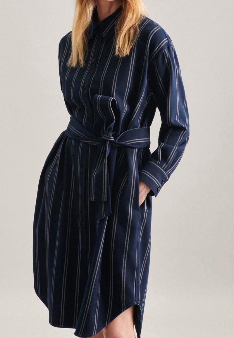 Mörkblå skjortklänning i mjukt tyg, med vertikala vita ränder, långa ärmar, knäppning med knappar och ett knytbart midjebälte.