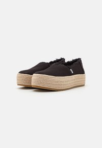 Baskets noires en toile à enfiler avec un bord effiloché, dotées d'une plateforme en jute et d'une semelle en caoutchouc, offrant un design décontracté.