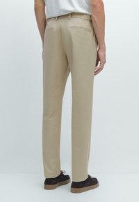 Pantalon beige, tissu léger, coupe droite, ceinture élastique, deux poches arrière, associé à des chaussures foncées. Pas de motifs ou d'accents notables.