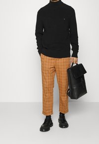 Svart ribbad polotröja, orange rutiga byxor, svarta tjocka snörskor och en svart läderryggsäck med klaff.