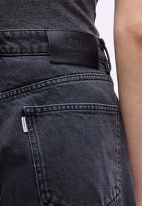 Κοντινό πλάνο στην πίσω τσέπη μαύρου γκρίζου τζιν με μαύρη δερμάτινη ετικέτα μάρκας "Mads Nørgaard Copenhagen" στη μέση