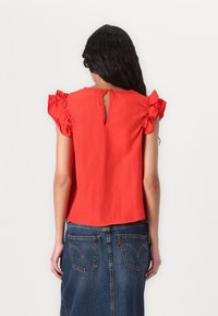 Rode blouse met korte mouwen en ruches, met een sleutelgatdetail aan de achterkant, gedragen met een denim A-lijn rok met achterzakken en zichtbare stiknaden.