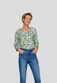 Bluse mit Blumenmuster in Grün und Blau mit Dreiviertelärmeln, kombiniert mit hochgeschnittenen blauen Jeans mit dekorativen Nähten.