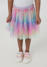 Gonna tutu nei colori pastello, con strati di tulle traslucido, vita arricciata e brillanti. Abbinata a sneakers rosa e bianche.