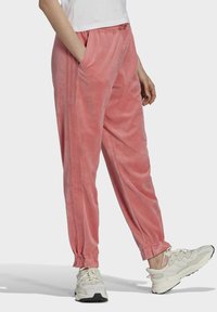 Rosa sammet joggers med sidfickor, elastiska muddarna och midja med dragsko. Stylad med vita sneakers med en texturerad design.