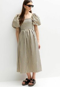 Vestido midi a rayas con mangas abullonadas en crema y negro, con escote cuadrado y corte relajado. Combinado con sandalias de plataforma negras.