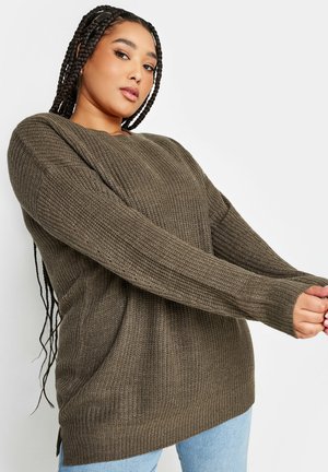 Olivgrüner Strickpullover mit Strukturmuster, langen Ärmeln, seitlichen Schlitzen und lässiger Passform, kombiniert mit hellblauen Jeans.
