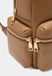 Zaino in pelle marrone texturizzata con doppie tasche con zip dorate, dotato di chiusure lisce e cuciture dettagliate lungo i bordi.