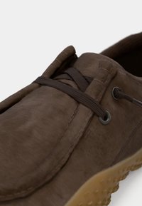 Zapato de cuero marrón con una textura suave, que presenta cordones marrones, ojales metálicos y una suela de goma flexible con un patrón de puntos.