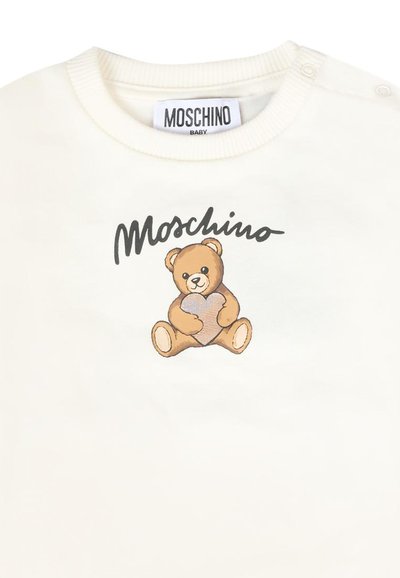 Felpa per neonati color crema con una grafica di un orsetto sorridente che tiene un cuore, con "Moschino" stampato sopra in nero.
