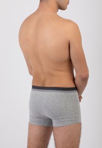 Boxer shorts grigi in cotone con vita scura e strisce bianche, mostrati da dietro su un modello senza camicia.