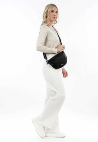 Black crossbody bag with a sleek design and zipper closure. The adjustable strap allows for comfortable wear. Worn by a model in neutral colors.