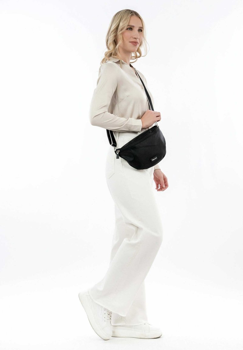 Black crossbody bag with a sleek design and zipper closure. The adjustable strap allows for comfortable wear. Worn by a model in neutral colors.