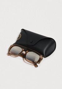 Καφέ διαφανή γυαλιά ηλίου με γκρι φακούς, τοποθετημένα πάνω σε μια μαύρη δερμάτινη θήκη με κούμπωμα και ανάγλυφο λογότυπο.