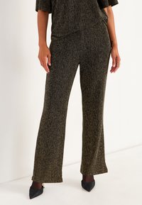 Svart- och guldtexturerade vida byxor med en subtil glans, som har en avslappnad passform och en mjuk midja. Matchas med spetsiga skor.