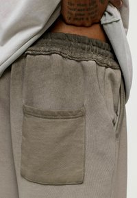 Lichtbruine joggers met een gestructureerde stof, elastische tailleband en een patchzak aan de zijkant. Casual ontwerp, zachte afwerking.