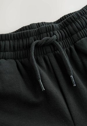 Černé tepláky s texturovaným elastickým pasem a šňůrkou, vyrobené z hladkého materiálu s vyztuženými konci na šňůrce.