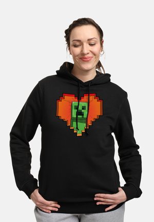 Zwarte hoodie met een pixelachtige hartontwerp in een oranje en groene kleurschema in het centrum, zachte stof en verstelbare trekkoorden.