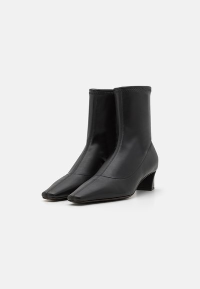 Botine negre din piele, cu vârf pătrat și toc mediu, având un design elegant și o textură netedă. Detalii cusute pe margini.