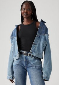 Giacca di jeans corta di colore azzurro, con chiusura a bottoni e due tasche frontali. Abbinata a una canotta nera aderente e jeans blu.
