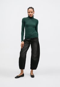 Σκούρο πράσινο μπλουζάκι με μακριά μανίκια και ψηλό γιακά, σετ με φαρδιά μαύρα τζιν και μαύρα μπαλαρίνες. Μαλακό ύφασμα με λεία υφή.