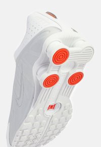 Tenisky Nike s převážně bílým a světle šedým designem, s červenými kruhovými akcenty na podešvi a texturovanou gumovou podrážkou.