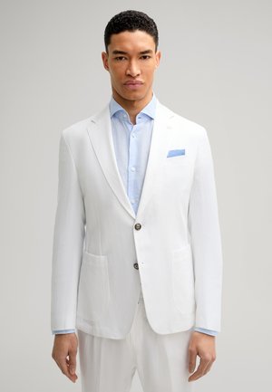 Weißer Leinenblazer mit zwei vorderen Taschen, Ein-Knopf-Verschluss, kombiniert mit einem hellblauen Hemd und einem blauen Taschentuch.
