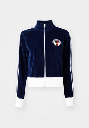 Giacca zip-up in velluto blu navy con colletto alto, strisce bianche sulle maniche e patch con logo sul petto. Presenta polsini e orlo bianchi.