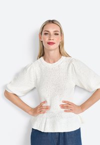Bílý texturovaný pletený top s krátkými nadýchanými rukávy, kulatým výstřihem a peplum spodním lemem. Látka má volné tkaní a měkký povrch.