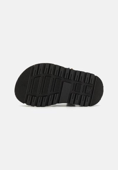 Semelle de chaussure en caoutchouc noir avec un motif texturé, comportant des côtes et des rainures pour une meilleure traction. Forme de bout arrondi et conception de base plate.