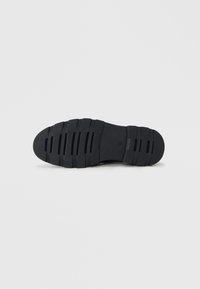 Suela de zapato de goma negra con ranuras horizontales y cortes verticales para mayor agarre. Punta redondeada y textura suave. Diseño ligero.