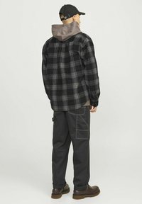 Geruite zwarte en grijze shirt met een grijze capuchon, gecombineerd met zwarte cargobroeken met witte stikselaccenten en bruine laarzen.