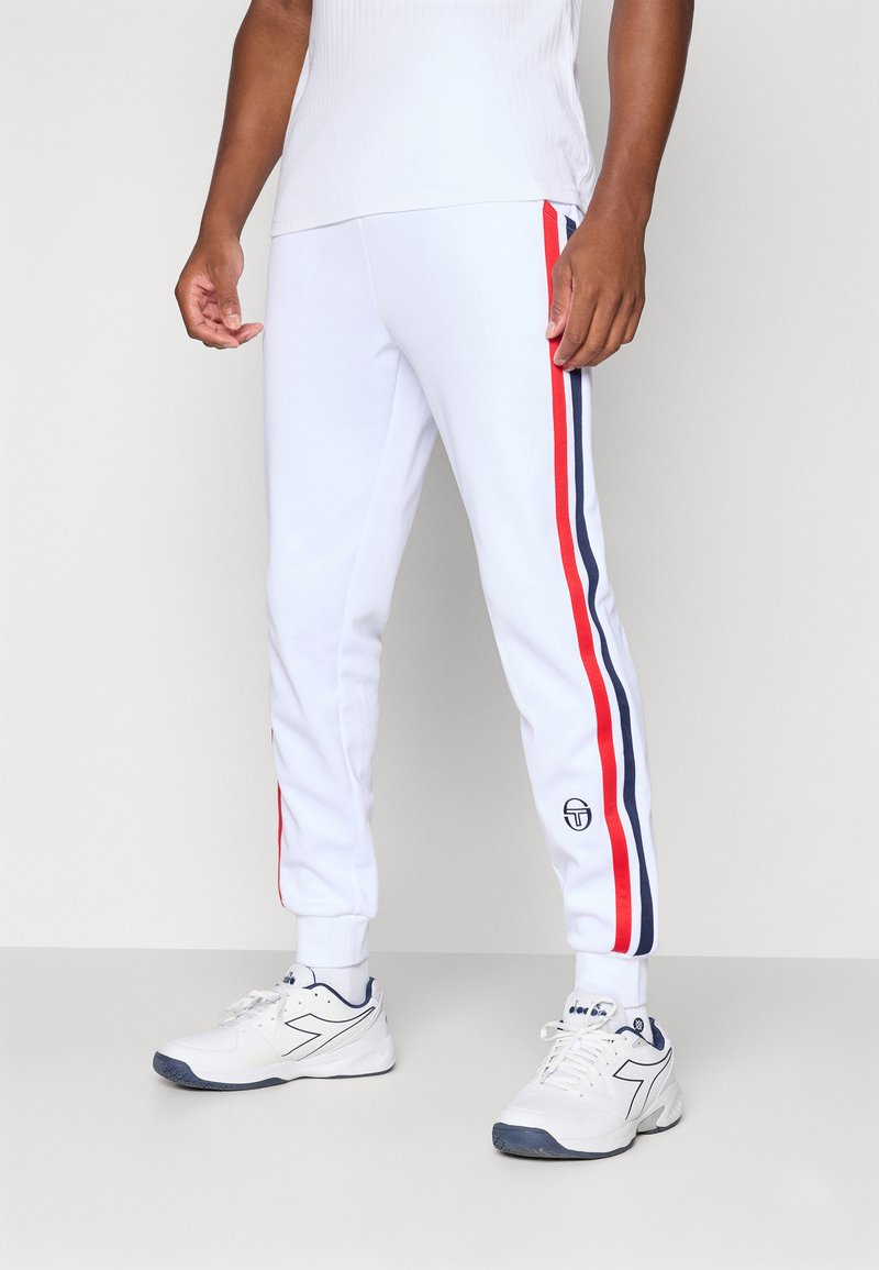 Vita joggers med röda och marinblå sidostreck, elastisk midja och ribbade muddarna. Logotypdetalj på vänster ben. Matchas med vita sneakers.