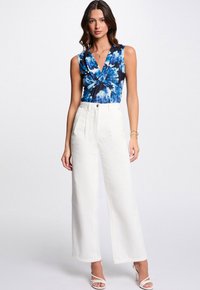 Bodysuit aus Baumwollmischung im blauen Batikmuster mit tiefem V-Ausschnitt; kombiniert mit weißen weiten Hosen, die vordere Falten und einen Knopfverschluss haben.