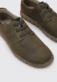 Zapatos de cuero marrón con diseño perforado, cierre de cordones y tacón en tono contrastante. Suela de goma texturizada con detalles cosidos.