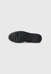Suela de zapato negra con superficie de goma texturizada, que presenta ranuras horizontales y verticales, bordes curvados y un área de talón reforzada.