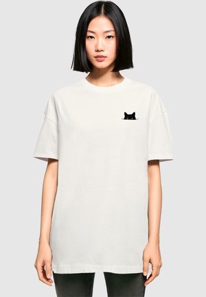 Weißes Baumwoll-T-Shirt mit einem schwarzen Katzendesign auf der linken Brust. Lockerer Schnitt mit kurzen Ärmeln und rundem Halsausschnitt.