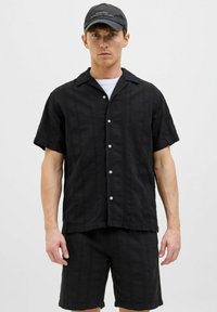 Svart kortärmad skjorta i texturerad tyg, framknäppning och matchande svarta shorts. Tillbehör inkluderar en svart keps med varumärkeslogotyp.