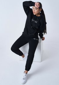 Sudadera negra y joggers a juego hechos de un material suave, con un bolsillo frontal y un logotipo. Combinados con zapatillas blancas.