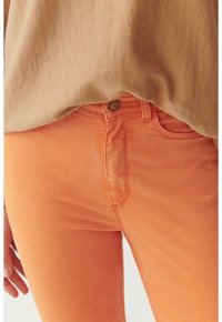 Narancssárga farmernadrág, elöl gombos záródással, diszkrét varrási részletekkel és Slim fit dizájnnal, bézs toppal párosítva.