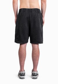 Calções atléticos pretos com cintura elástica, costura visível e ajuste descontraído, combinados com ténis cinzentos para funcionalidade.