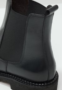 Botín de cuero negro con paneles laterales elásticos, acabado mate texturizado y suela de goma gruesa, que presenta costuras a lo largo del borde.