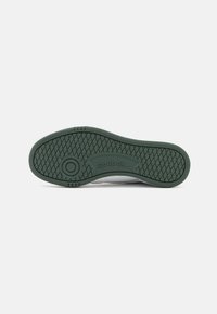 Reebok tenisice s teksturiranom zelenom gumenom podlogom, koja uključuje uzorčasti dio za grip i utisnuti brend sa strane.