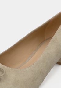 Gros plan sur une chaussure femme en daim beige à petit talon montrant un bout arrondi, une texture douce et une doublure intérieure beige.